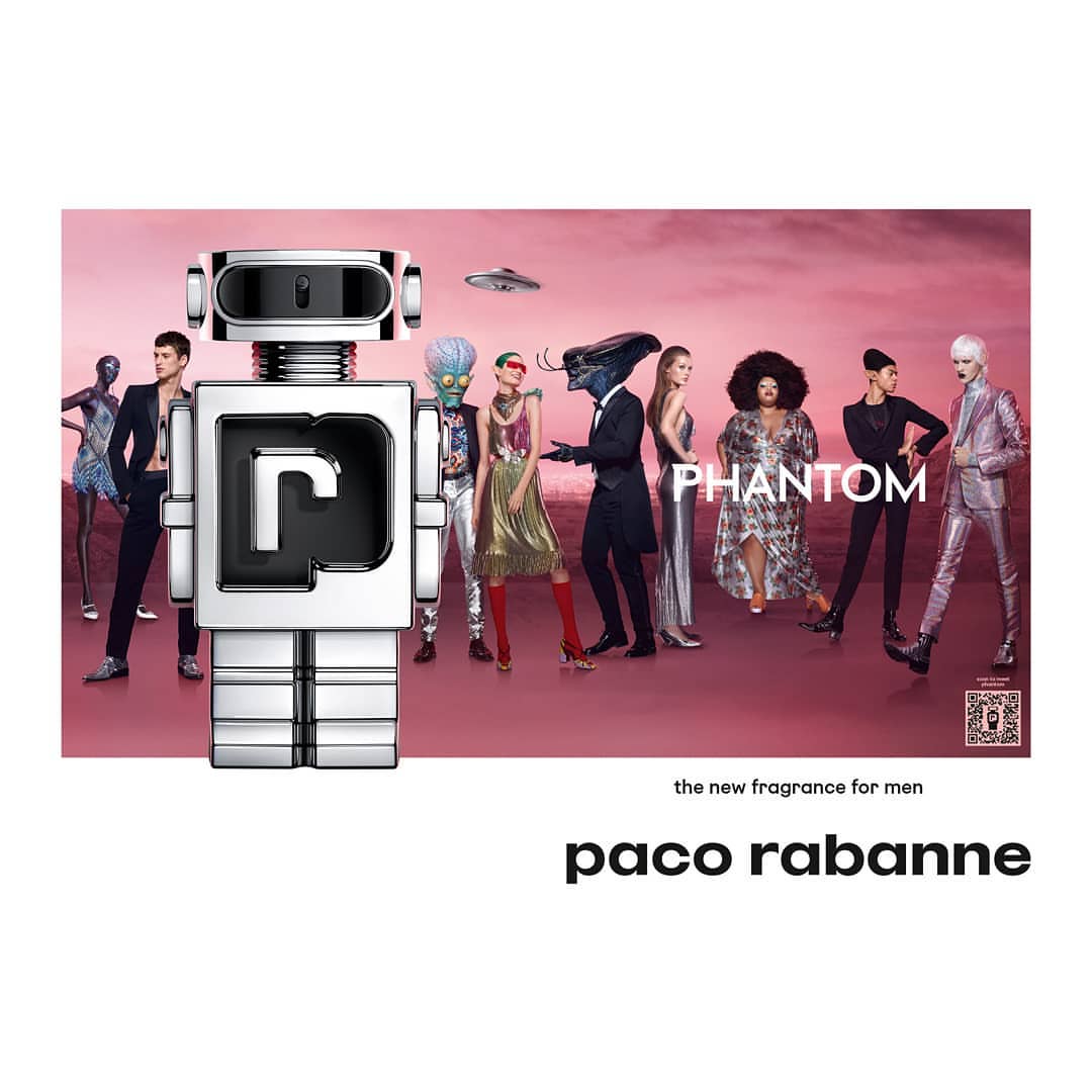 Robot-shaped Paco Rabanne Phantom perfume bottle among group of people against a pink background with a flying saucer image.