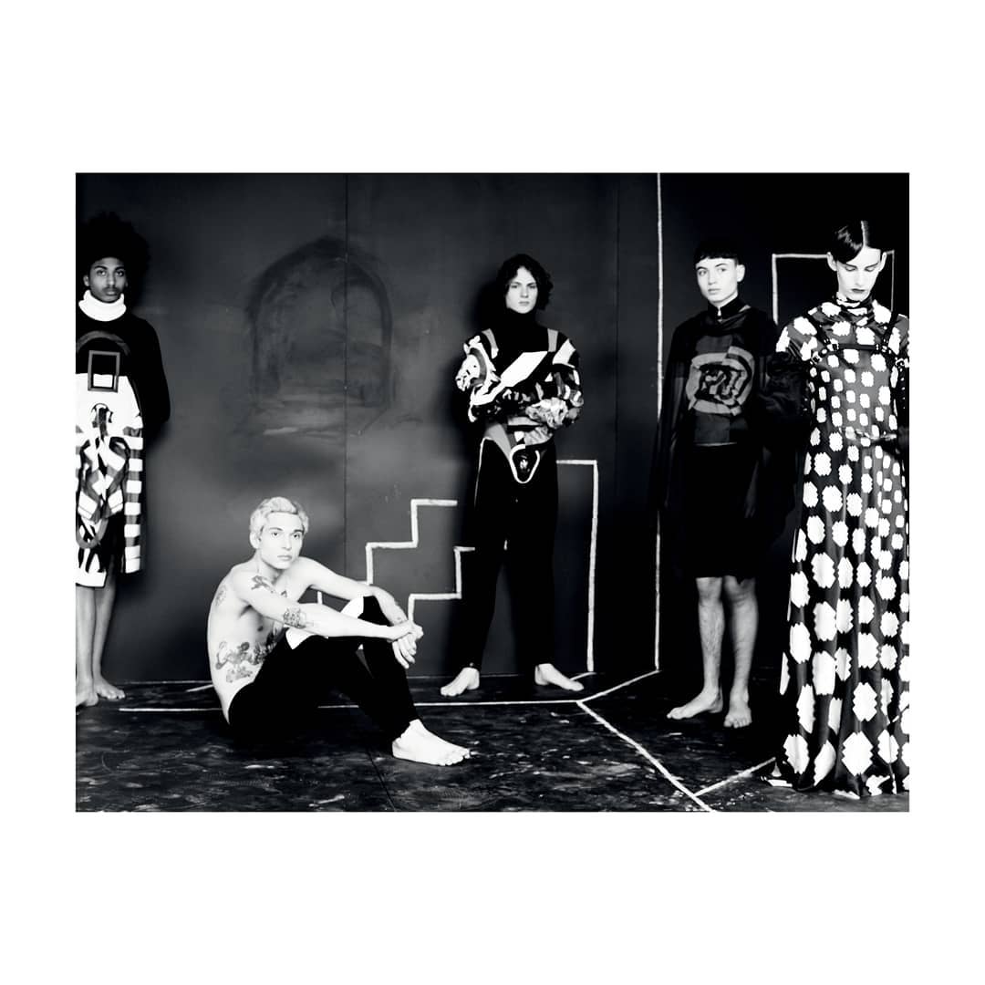 Monochrome fashion shot of five people wearing avant-garde black-and-white patterned outfits posing in a photo studio setting.