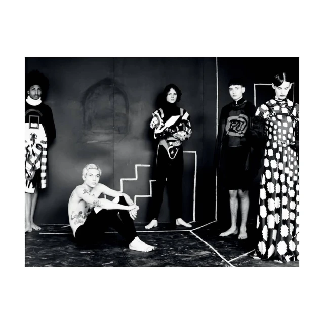 Monochrome fashion shot of five people wearing avant-garde black-and-white patterned outfits posing in a photo studio setting.