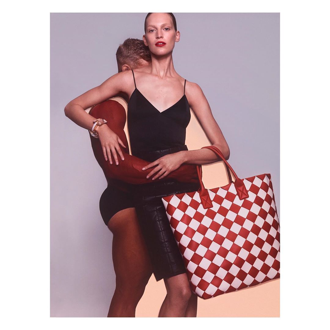 Two fashion models in a photo studio, an adult female and an adult male, the female is holding a checkerboard pattern tote bag.