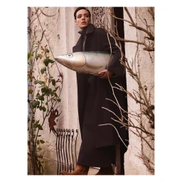 Short-haired woman in a dark coat holding a large fish inflatable standing in a doorway