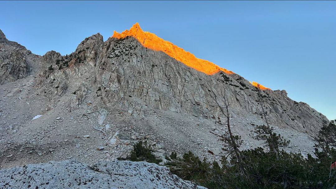 Scenic view of a tall, rocky mountain partially illuminated by golden sunlight against a clear blue sky on a sunny day outdoors.