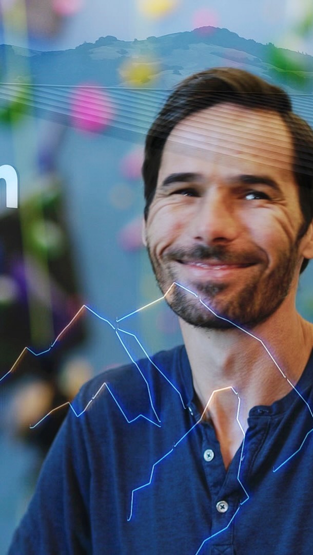 Portrait of a smiling adult male in a blue shirt, with mountain landscape and data visualizations overlaid. Warm studio lighting.