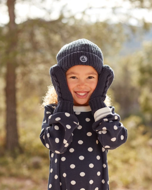 Happy young girl wearing knitted hat and mittens with polka dot dress, outdoors in natural light with blurred background.