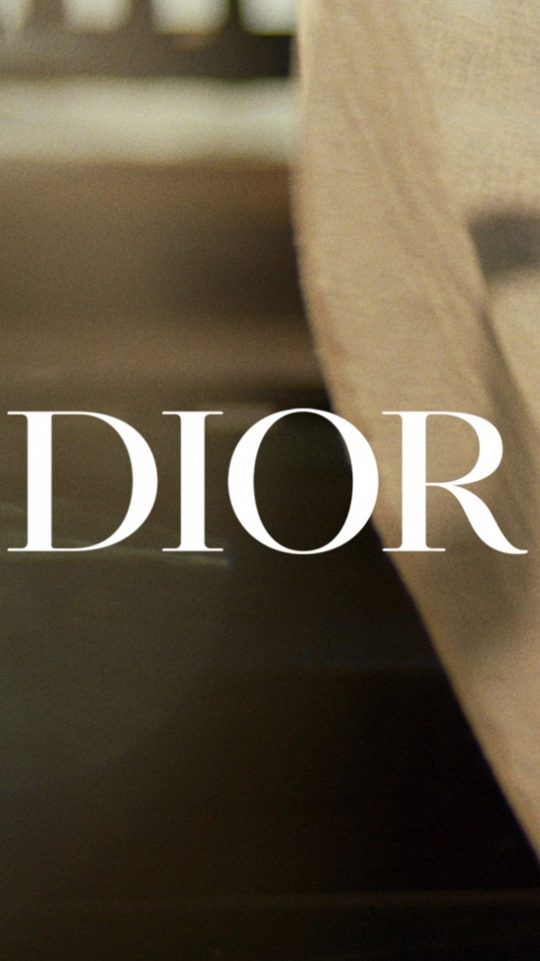 Close-up of Dior logo in vertical format, featuring a blurred figure and dark background, for fashion or luxury brand aesthetic.
