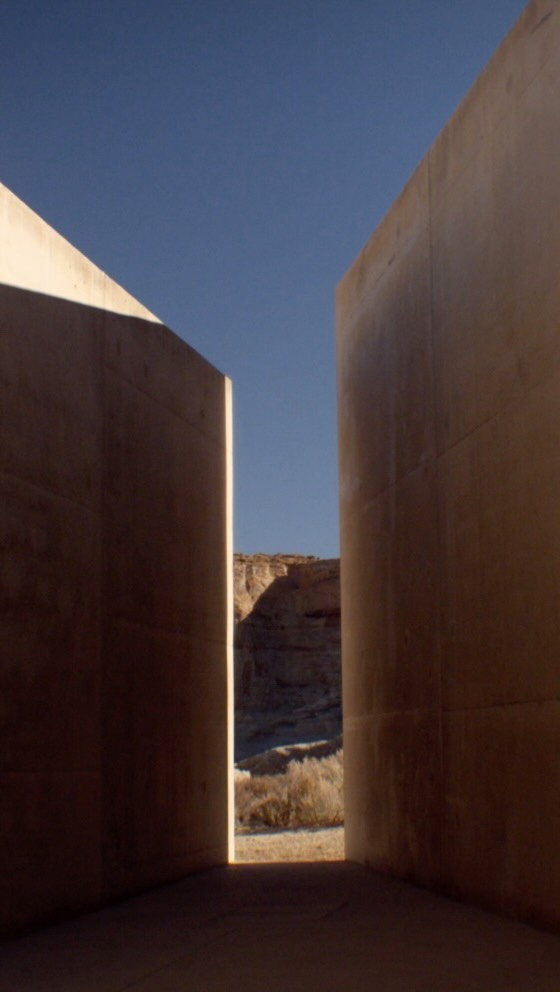 Architectural view of desert landscape through minimalist geometric structures, featuring clear blue sky and sandy ground.