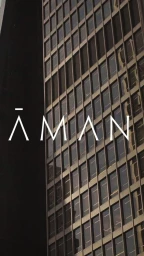 Close up shot of a modern skyscraper facade with a grid of windows under warm light, featuring the word AMAN in white type.