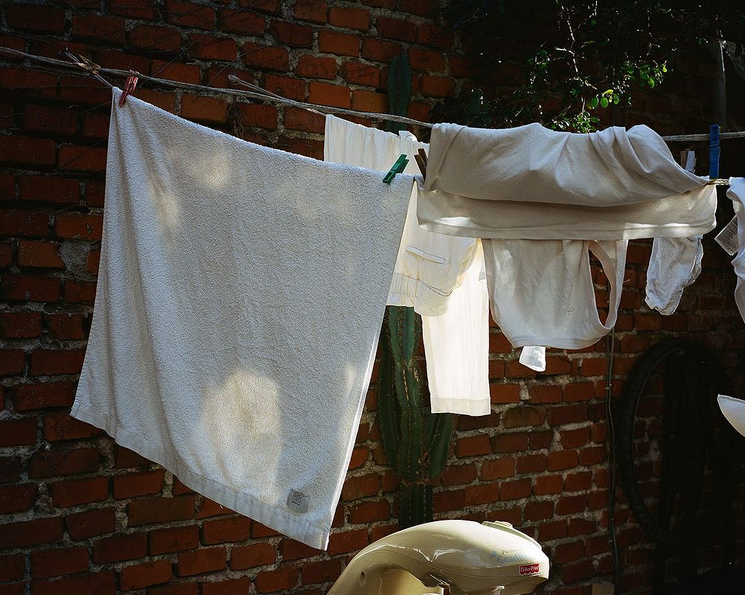 Various clean white laundry items hanging outside on a clothesline in front of a rustic brick wall, with a cactus in the background.