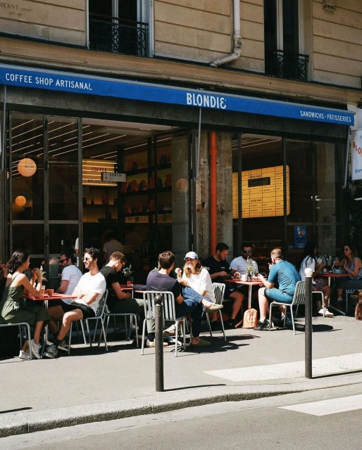 Outdoor cafe in Paris with a group of people sitting at tables and enjoying coffee on a sunny day in an urban setting.