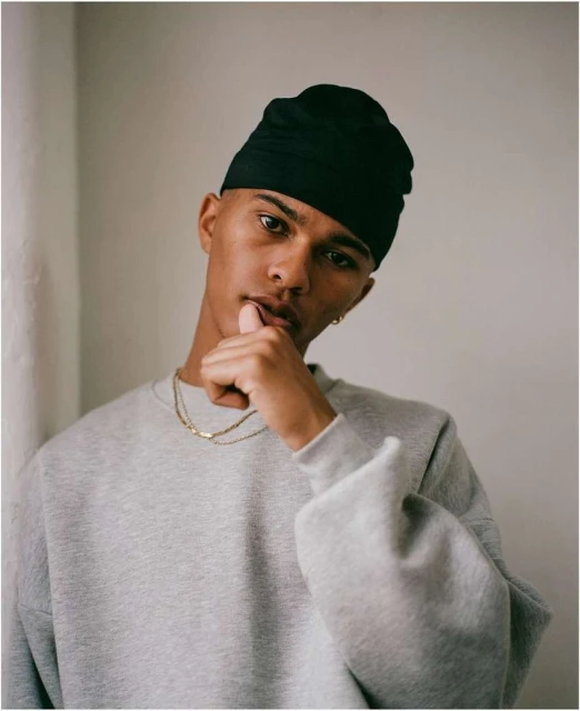 Portrait of a young adult male wearing a black beanie and grey sweatshirt, indoors, looking at the camera with a neutral expression.