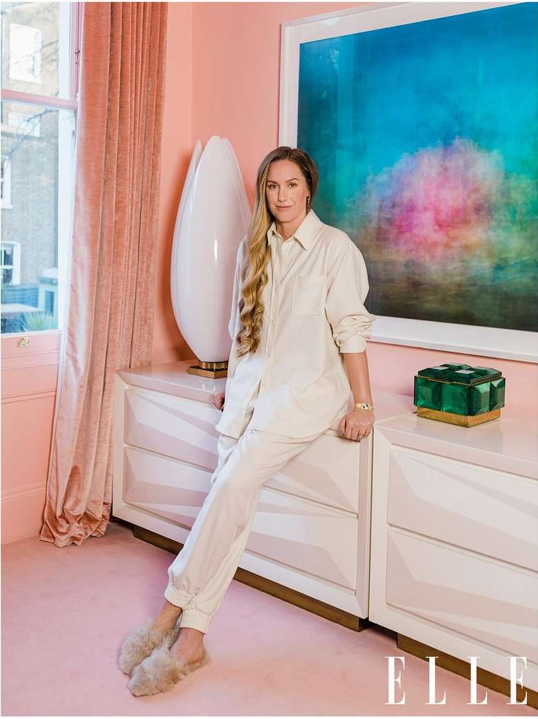 Woman in cream-colored outfit poses in interior with pink walls, white dresser, art, and ELLE magazine logo in foreground.