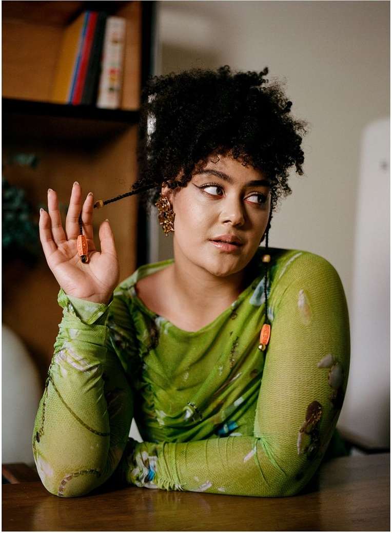 Portrait of a woman with dark curly hair wearing a sheer green patterned top, photographed in London by Vicky Grout.