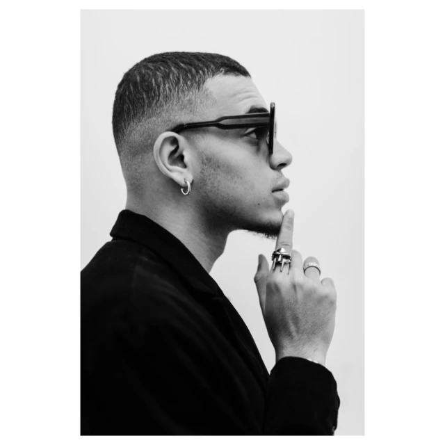 Portrait of adult male in profile wearing sunglasses and rings in black and white. Man with buzzcut, looking to the right.