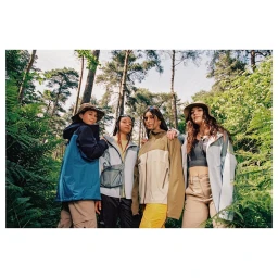 Four women in outdoor jackets and hats standing together in a forest, photographed from a low angle by Vicky Grout.