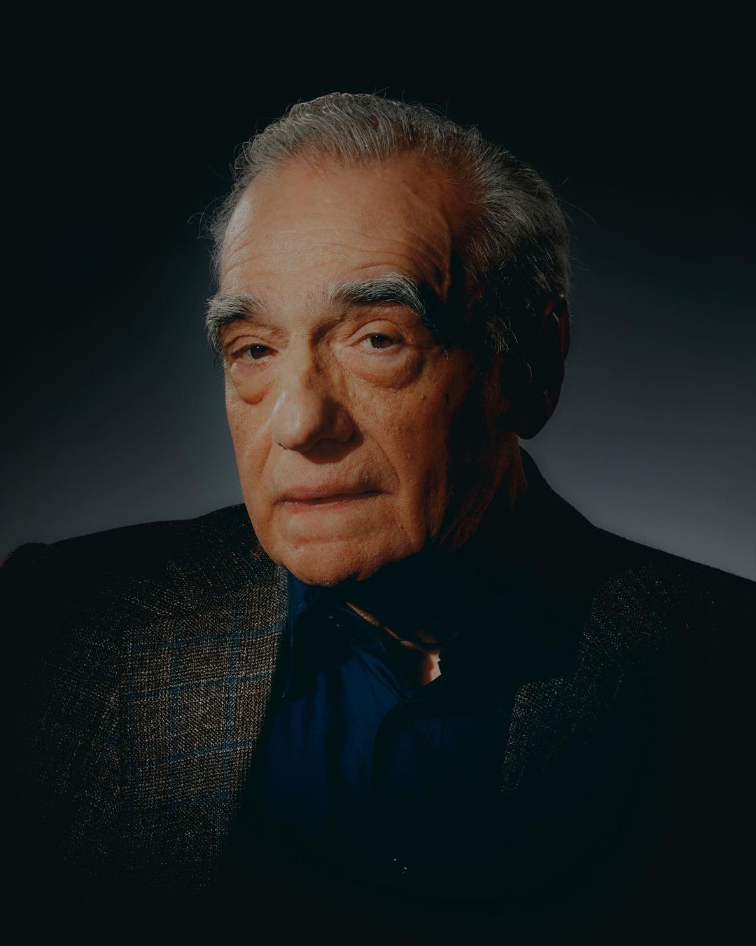Portrait of a distinguished older gentleman with gray hair wearing a dark suit and blue shirt, captured in soft, directional studio lighting.