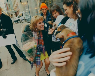 A smiling woman holding a bouquet of roses and greeting puppies on a city street, captured by Victor Llorente in New York.