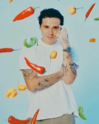 Portrait of Brooklyn Beckham wearing a white t-shirt surrounded by floating red and yellow chili peppers