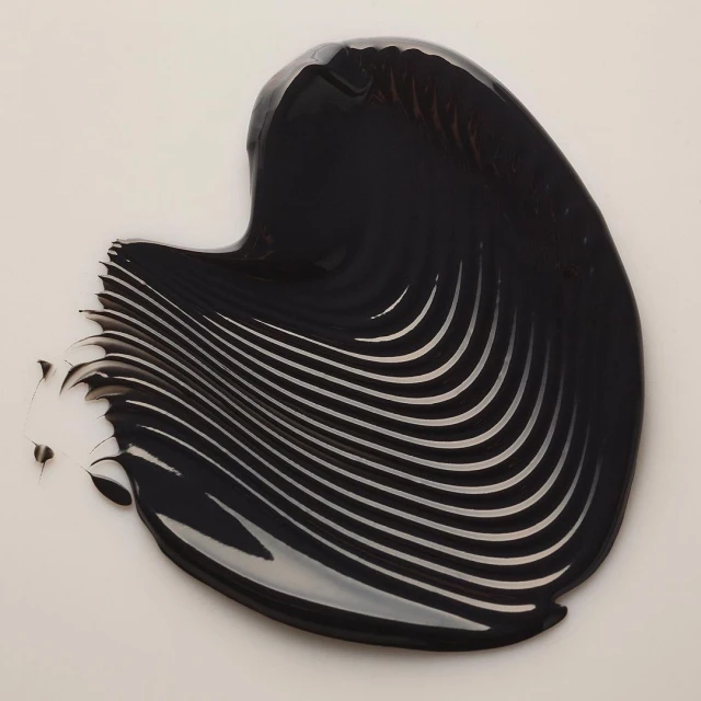 Dark, glossy liquid with a ribbed texture is spread across a pale background, creating an abstract pattern with a smooth and shiny surface.