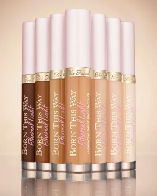 Assortment of 'Born This Way Ethereal Light' concealer tubes in various skin tones, lined up against a neutral background, beauty product.