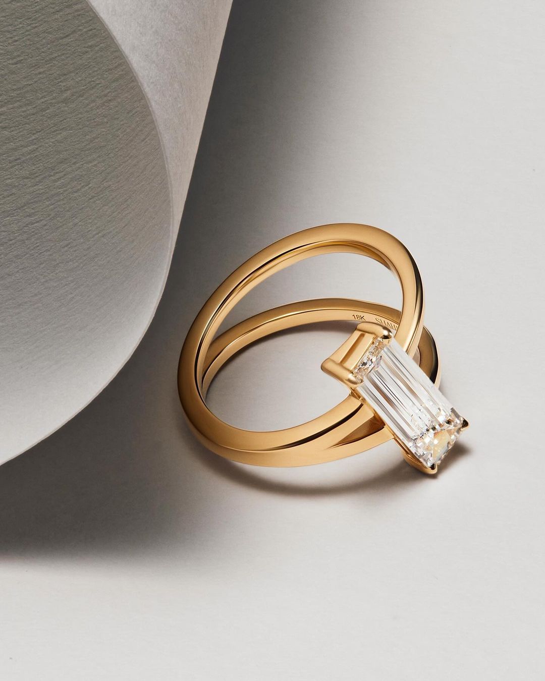 Close-up studio shot of a gold ring featuring a rectangular diamond, set against a light grey background, showcasing jewelry design.