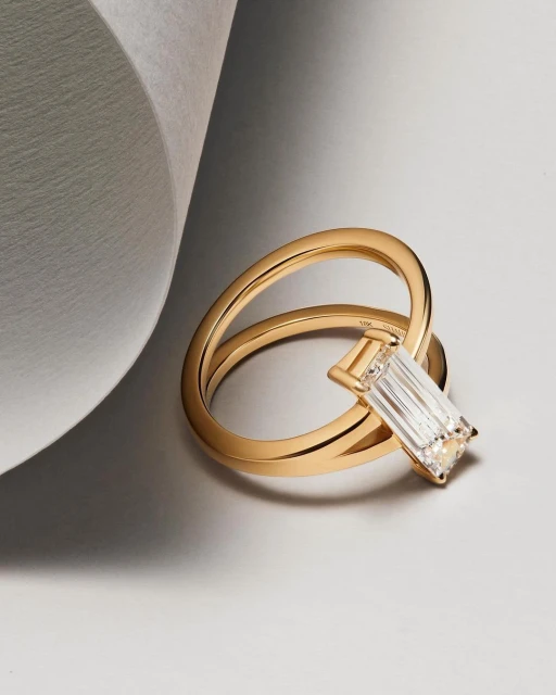 Close-up studio shot of a gold ring featuring a rectangular diamond, set against a light grey background, showcasing jewelry design.
