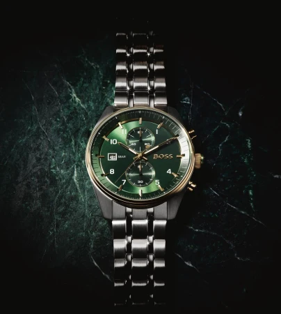 Close-up studio shot of a Hugo Boss wristwatch with a silver band and a green dial on a dark green, veined marble surface.