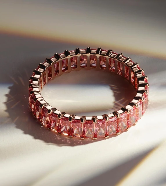 Close-up of a pink eternity ring featuring pink gemstones set in a band of rose gold. Jewellery shot in studio lighting.
