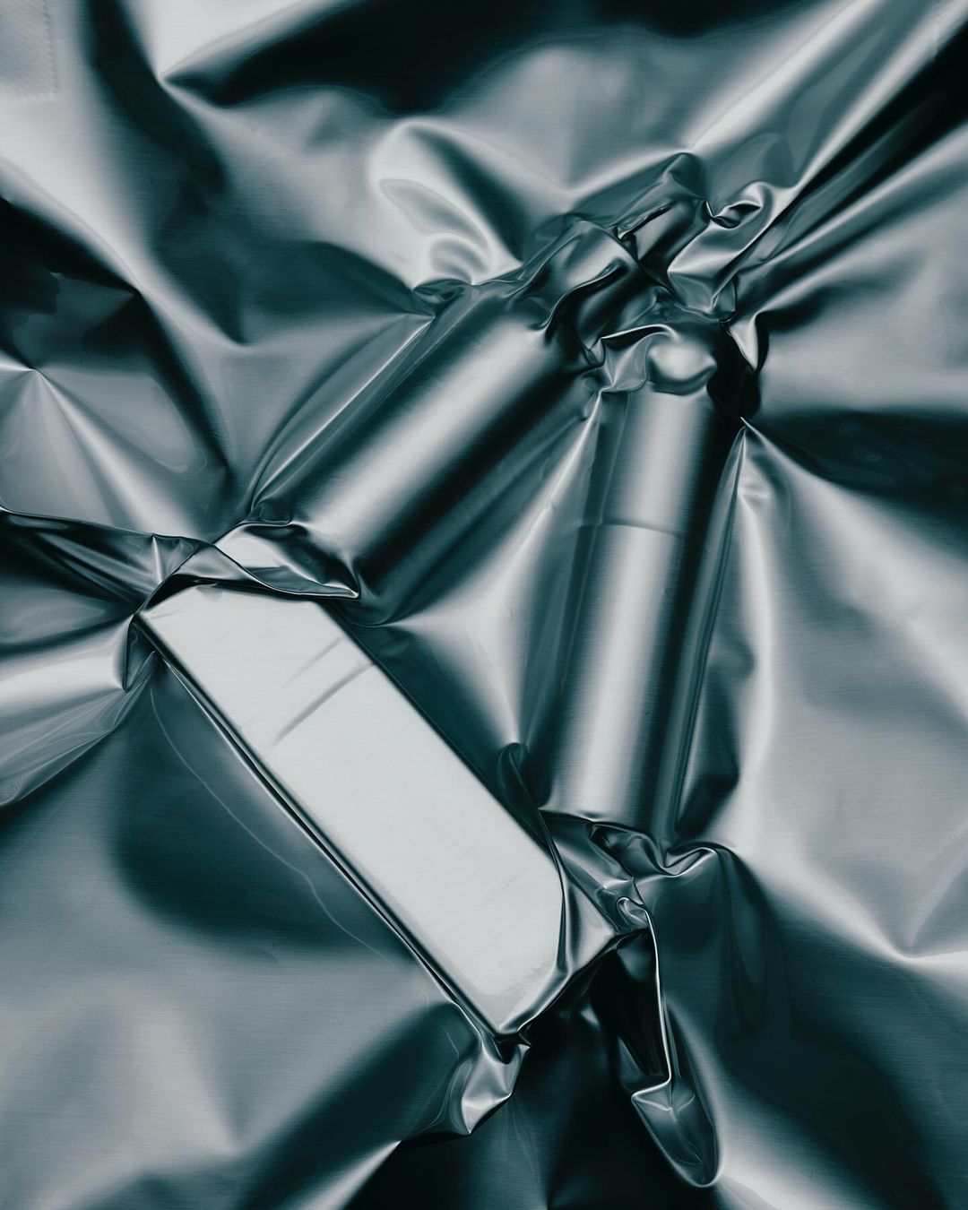 Shiny rectangular objects on crumpled silver wrapping, creating a dynamic play of light and shadow.