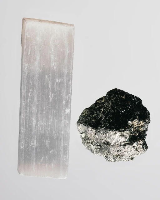 A selenite crystal and pyrite specimen rest on a light gray surface, showcasing their distinct textures and colors.
