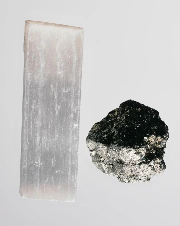 A selenite crystal and pyrite specimen rest on a light gray surface, showcasing their distinct textures and colors.