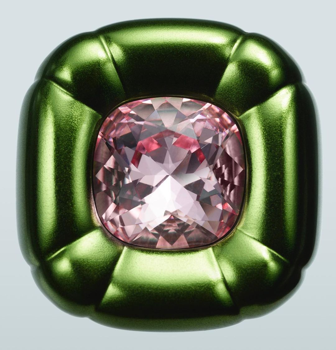 Cushion-cut morganite gemstone is set in a green metal mounting. The gemstone is faceted and light pink in color. The mounting is shiny.
