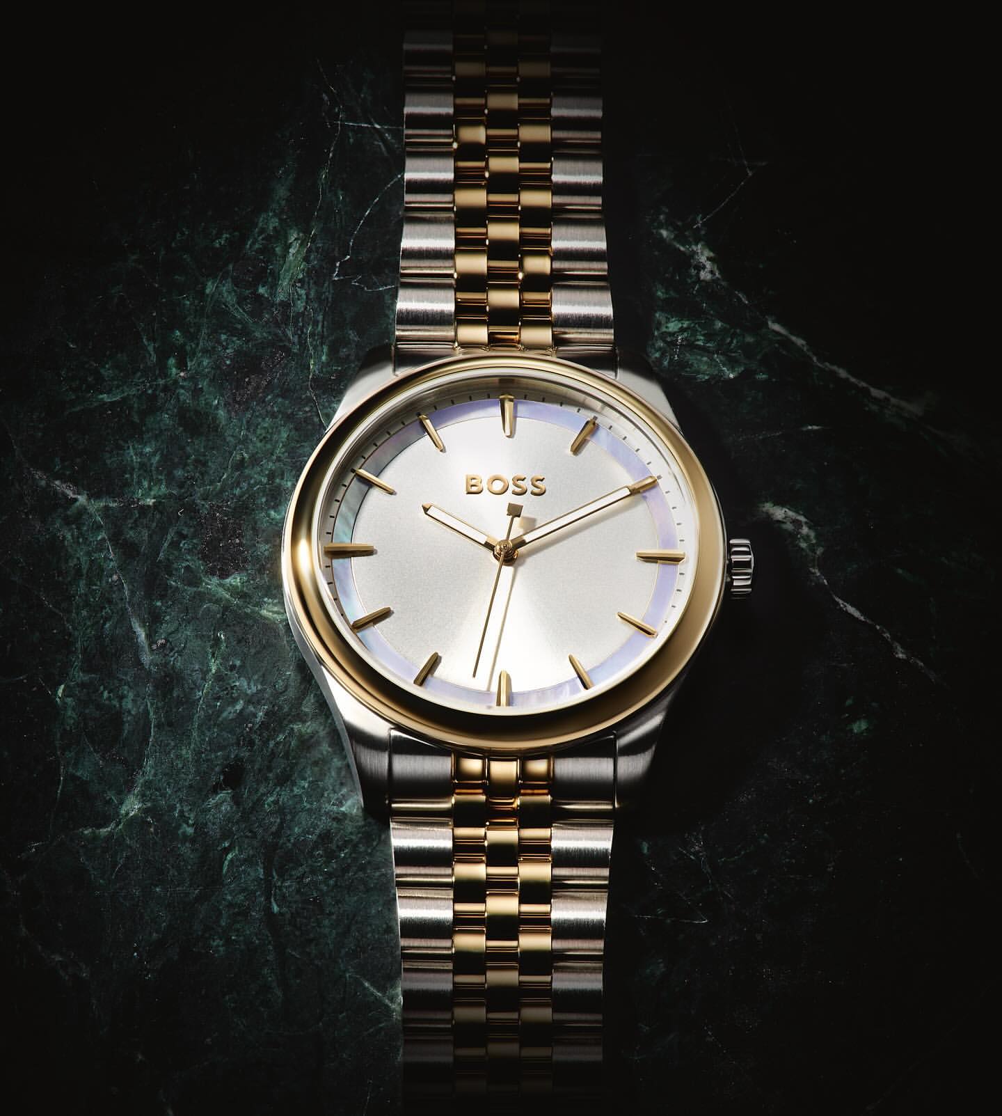 Close-up studio shot of a two-tone stainless steel and gold Hugo Boss wristwatch on a mottled dark green marble surface.