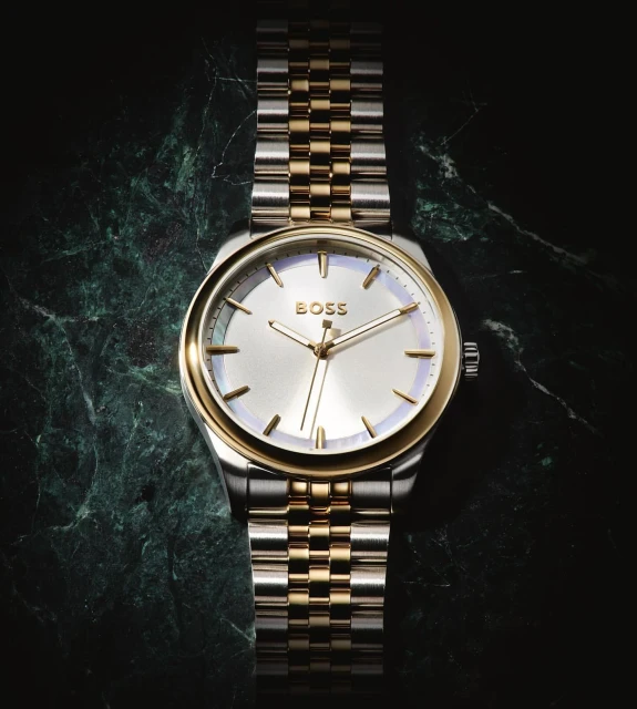 Close-up studio shot of a two-tone stainless steel and gold Hugo Boss wristwatch on a mottled dark green marble surface.