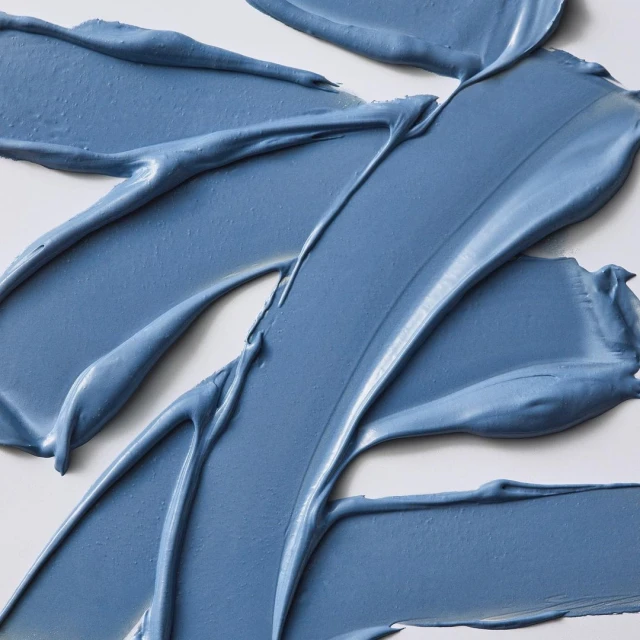 Close-up of thick blue cosmetic cream or clay spread across a white background, showcasing texture and vibrant color.