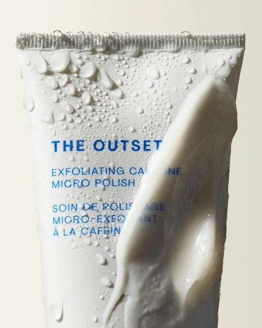 White tube of The Outset exfoliating caffeine micro polish, brand name visible, with water droplets and a dollop of cream.