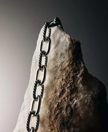 Silver cable chain necklace draped over a rough light-colored stone against a dark gradient background