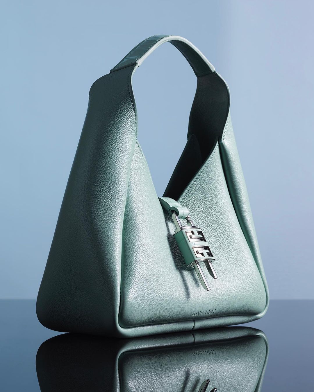 Light blue Givenchy handbag with silver logo hardware, photographed in a studio setting with a reflective black surface and light blue background.