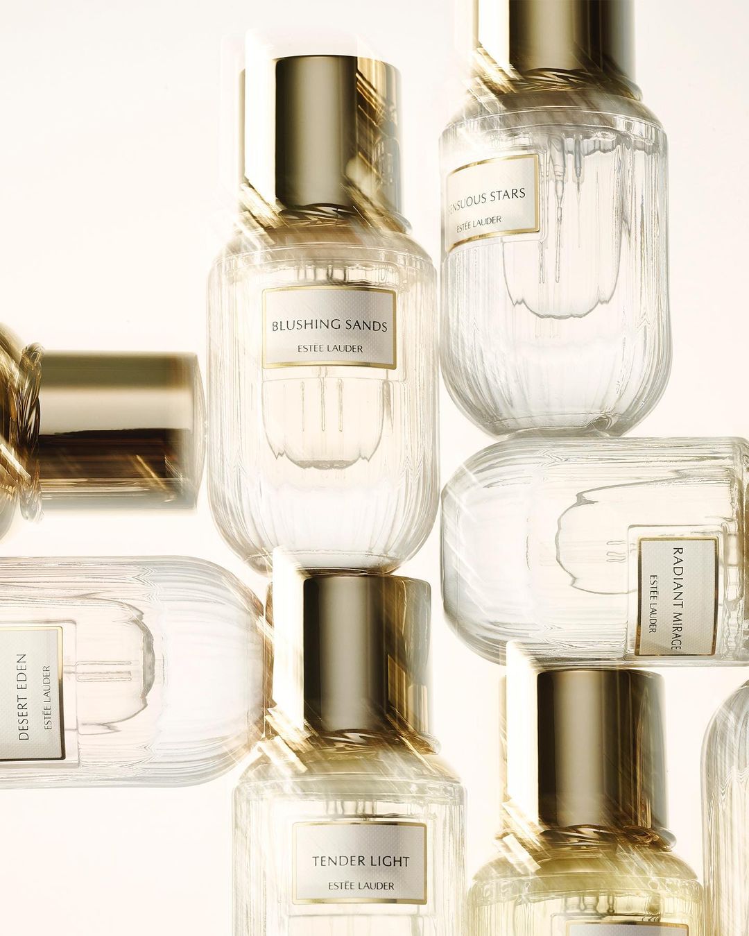 Close-up of multiple clear glass perfume bottles with gold caps and labels in a studio setting, showcasing beauty product photography.