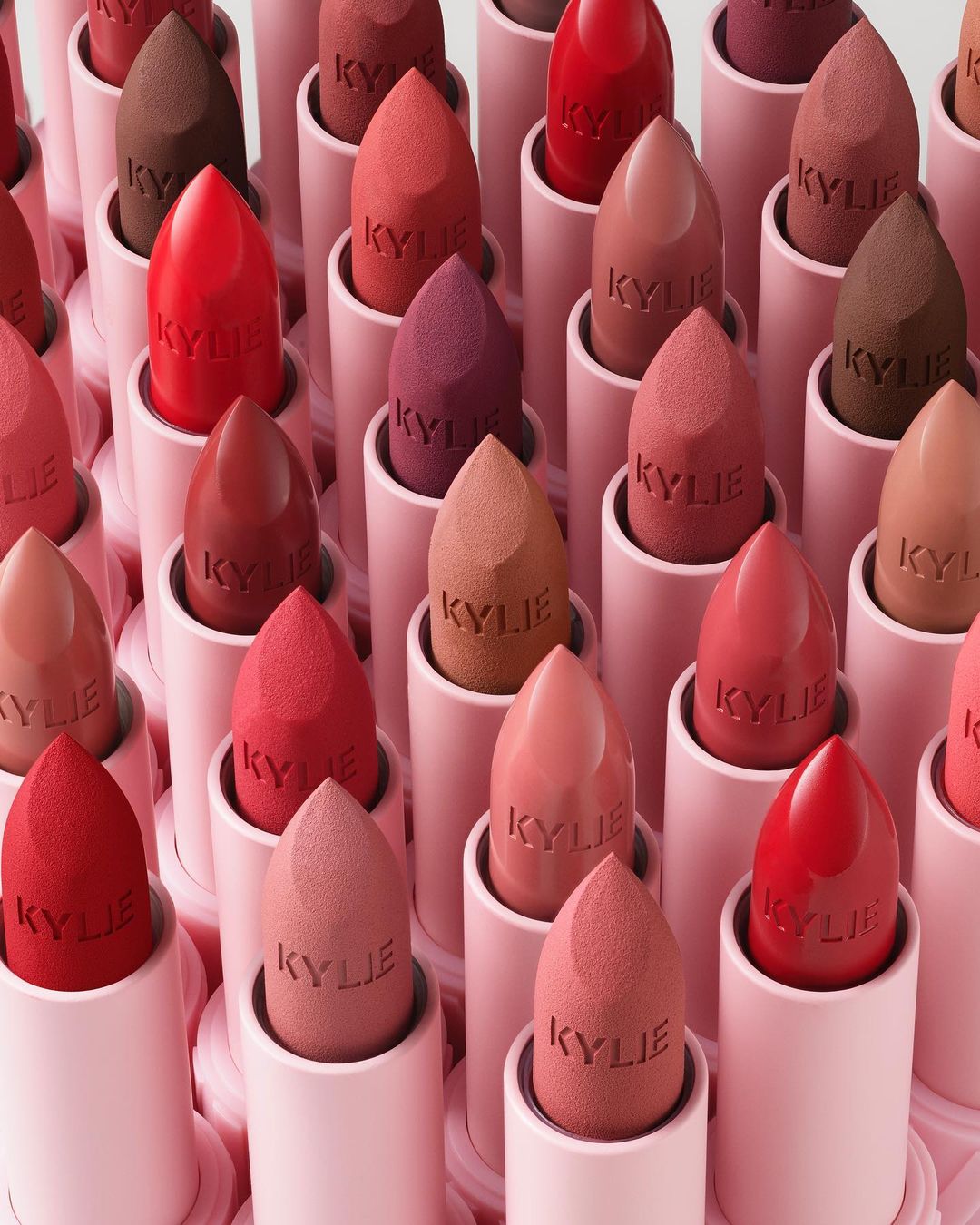 Close-up of multiple Kylie lipsticks in pink tubes with sponge applicators showing various nude, red, and brown shades.