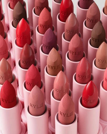 Close-up of multiple Kylie lipsticks in pink tubes with sponge applicators showing various nude, red, and brown shades.