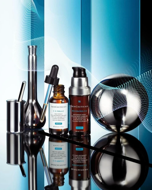 Still life shot of SkinCeuticals skincare products including C E Ferulic and Resveratrol B E, displayed on a reflective surface.