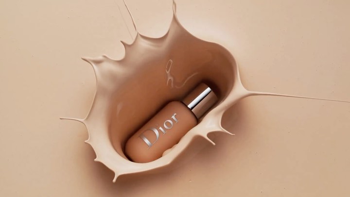 Dior foundation bottle is surrounded by splashing beige liquid in an eye-level studio shot, capturing a beauty and cosmetic product.