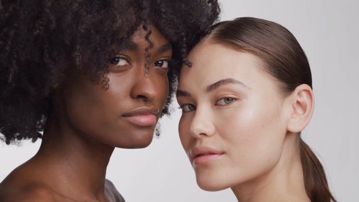 Close-up portrait of two diverse female models with natural makeup posing closely against a neutral white background.
