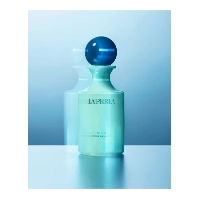 Close-up studio shot of La Perla Villa Sorrento perfume bottle with a blue spherical top, set against a gradient blue background.