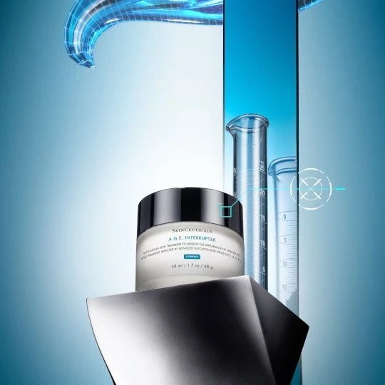 A jar of Skinceuticals A.G.E. Interrupter cream sits on a shiny platform, flanked by lab beakers against a gradient blue backdrop.