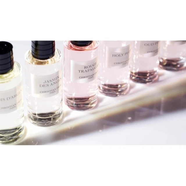 Close-up of several clear glass perfume bottles with black caps on a white surface with shadows creating depth and detail.