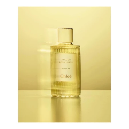 Elegant still life showcases a glass bottle of Chloé Atelier des Fleurs Verbena perfume against a gradient golden background.
