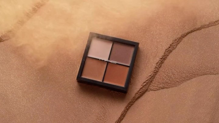 Close-up of a four-shade makeup palette, featuring neutral and earthy tones, displayed on a textured, shimmering bronze surface.