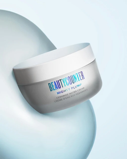 Beautycounter Mighty Plump Ceramide Water Cream jar against a light blue background with soft, rounded abstract forms.