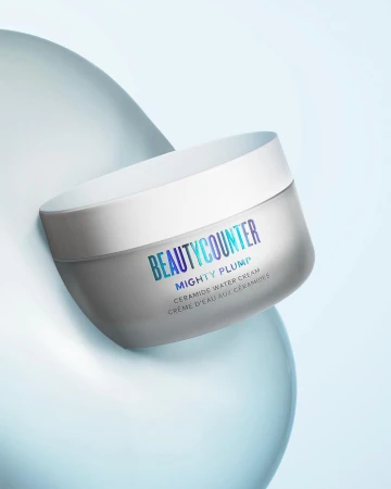 Beautycounter Mighty Plump Ceramide Water Cream jar against a light blue background with soft, rounded abstract forms.